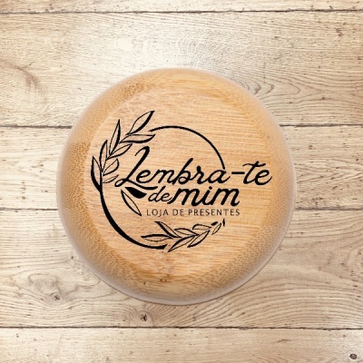 Tábua redonda de madeira clara com gravação 'Lembra-te de mim LOJA DE PRESENTES' e folhas em padrão