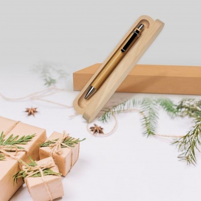 Caneta de madeira numa caixa de madeira com presentes e ramos de Natal ao fundo