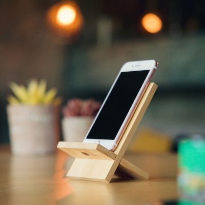 Suporte de telemóvel em madeira claro numa mesa com fundo desfocado