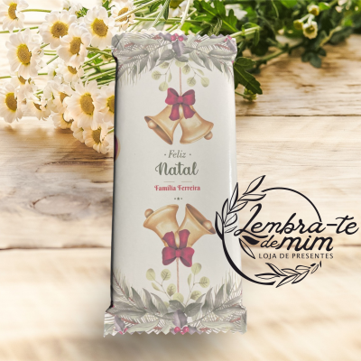Barra de chocolate embrulhada com tema de Natal numa mesa de madeira com flores e logo da loja