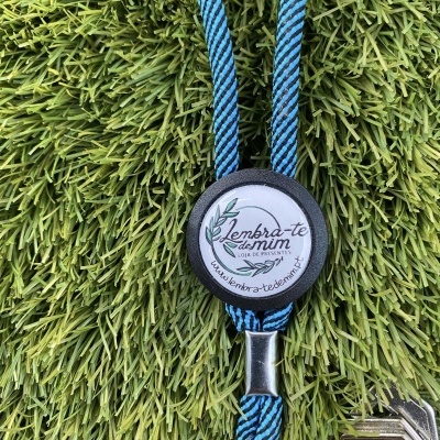 Chaveiro azul e preto com símbolo e texto, sobre relva artificial