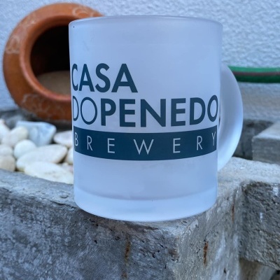 Caneca de vidro fosco branca com texto preto em superfície de pedra com vaso e pedras ao fundo