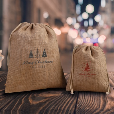 Dois sacos de juta com motivos natalinos e texto impresso, em superfície de madeira, fundo desfocado