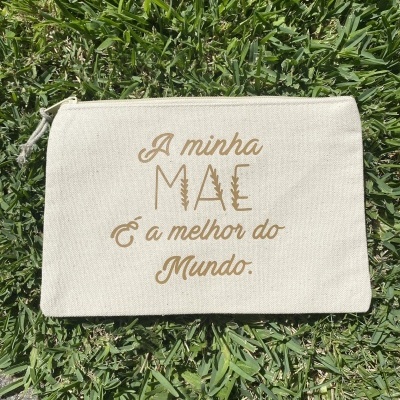 Necessaire de tecido bege com texto dourado sobre relva verde