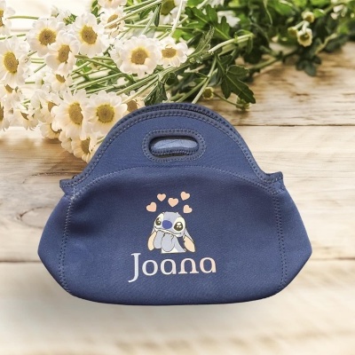 Bolsa pequena azul com desenho e nome 'Joana' junto a flores brancas