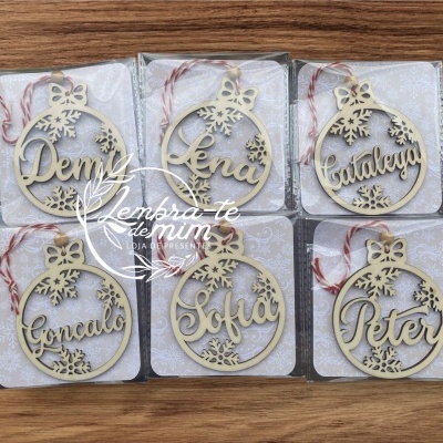 Ornamentos de Natal redondos em madeira clara com nomes personalizados e flocos de neve, em fio vermelho e branco, sobre fundo de madeira.