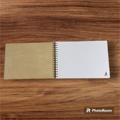 Caderno espiral aberto com capa castanha e folhas brancas numa superfície de madeira