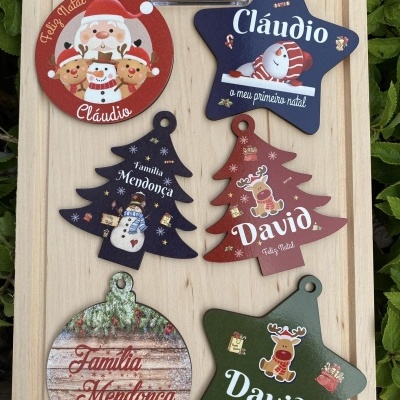Ornamentos natalinos de madeira com nomes e ilustrações festivas em várias formas e cores