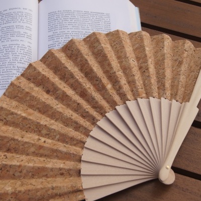 Leque de cortiça com madeira clara e texto 'Artes Mistas', sobre mesa de madeira ao lado de um livro aberto