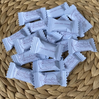 Balas embrulhadas em papel branco com texto 'Lembra-te de mim' e website, sobre superfície de palha trançada