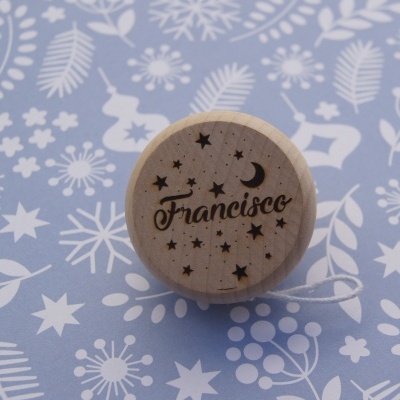 Ioiô de madeira gravado com nome e estrelas sobre fundo azul com padrão branco