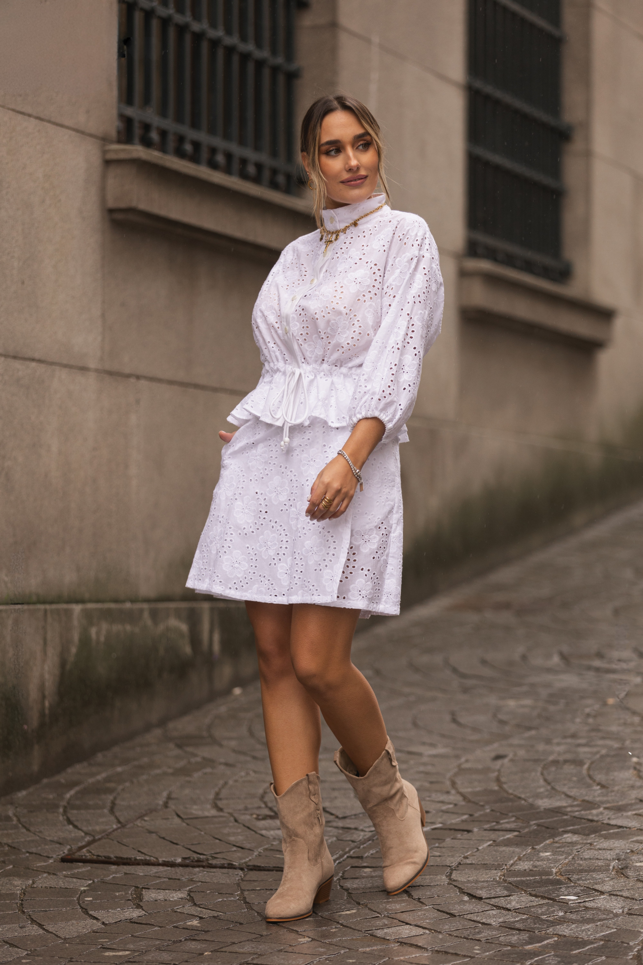 Calção Saia Branco Bordado Inglês Cintura Alta com Bolsos Miss You Vestido branco rendado com padrão floral e botas bege em rua de pedra