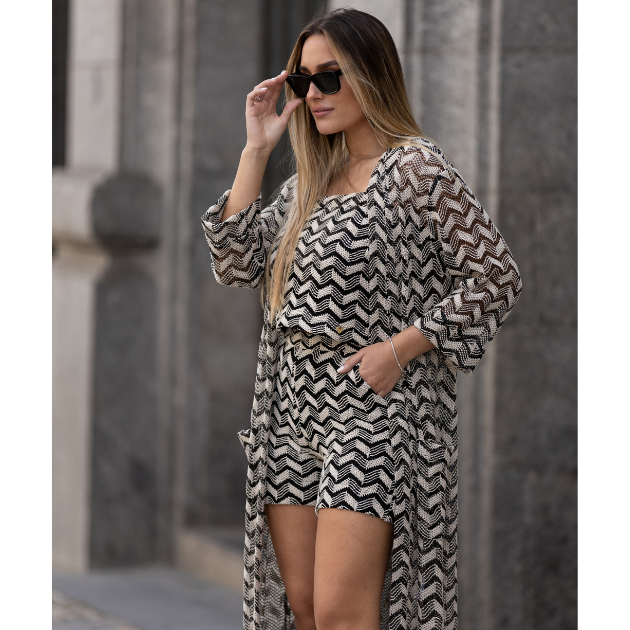 Calção feminino preto e branco Miss You Conjunto feminino com padrão geométrico preto, branco e bege, composto por top, calções e capa longa transparente, num ambiente urbano.