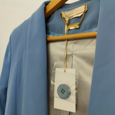 Casaco azul claro com etiqueta ALBERTA FIAGI e botão pendurado num cabide