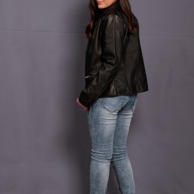 Menina com casaco de couro preto e calças de ganga posando de perfil