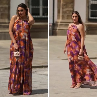 Mulher a desfilar com vestido longo colorido e mala pequena em cenário urbano