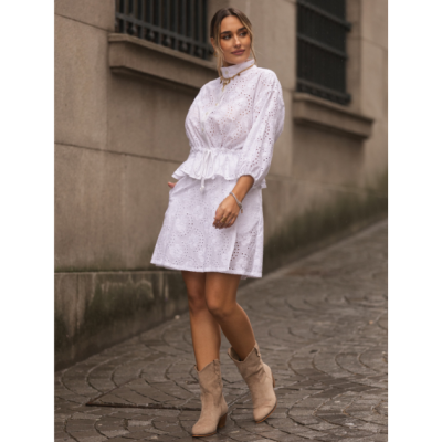 Mulher vestindo vestido branco de algodão bordado com botas bege, em passeio urbano com calçada de pedra.