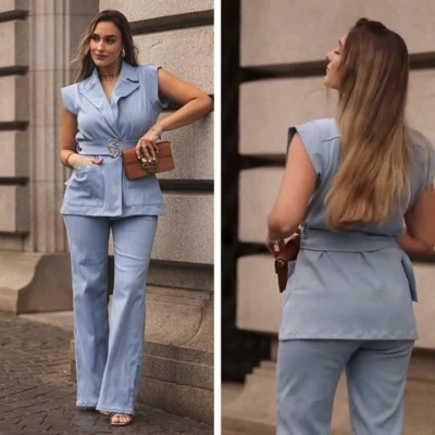 Mulher a vestir fato azul claro com casaco sem mangas e calças largas segurando uma carteira castanha.