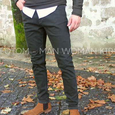 Pessoa vestindo calças pretas, camisa branca e camisola cinza, em chão de pedra com folhas secas