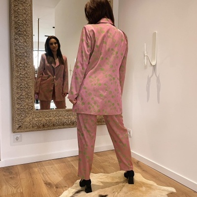 Conjunto feminino rosa com flores verdes refletido em espelho num quarto com chão de madeira