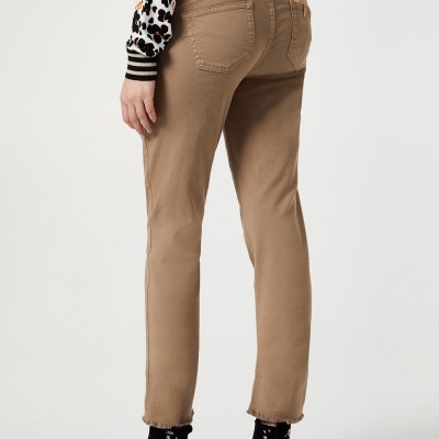 Calças bege justas com bainha irregular e cinto, botas pretas com detalhes metálicos, blusa estampada, fundo branco