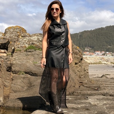 Mulher com vestido preto em couro e rede junto a rochas e mar