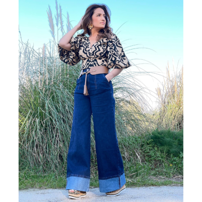 Mulher com calças de ganga largas, blusa padrão animal e sapatos de cunha em ambiente ao ar livre