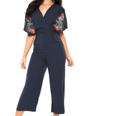 Macacão azul escuro com bordados florais nas mangas usadas por mulher com sandálias de salto