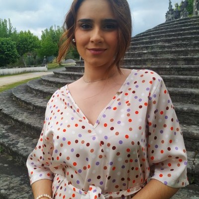 Blusa bege claro com bolinhas roxas e laranjas usada por mulher em escadaria de pedra