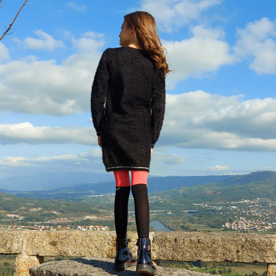 Criança de costas com casaco preto e leggings cor de rosa e pretas em paisagem montanhosa