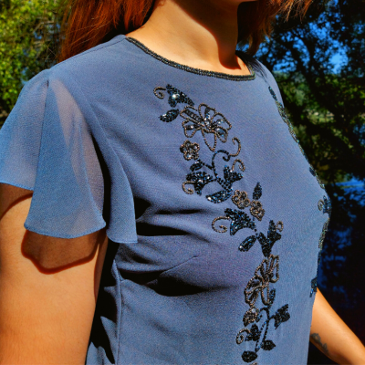 Blusa azul feminina com bordados florais e mangas transparentes, usada ao ar livre