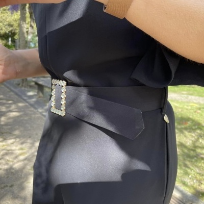 Cinto preto com fivela de pérolas num vestido ou saia preta em ambiente exterior