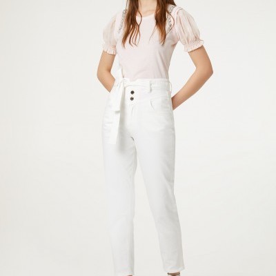 Mulher a usar calças brancas com cinto, t-shirt rosa pálido de manga curta bufante e botins brancos com bolinhas pretas