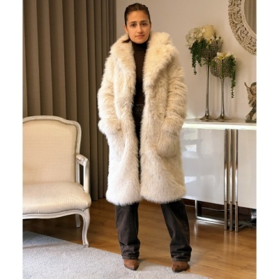 Mulher a usar casaco de pêlo branco creme junto a cadeira e móvel em ambiente interior