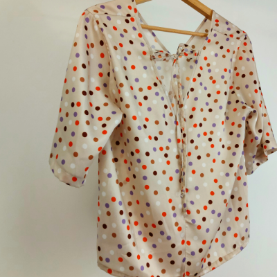 blusa bege com bolinhas coloridas e laço na parte traseira pendurada