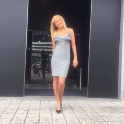 Mulher a usar vestido justo cinza com alças finas em frente a parede preta com porta vidro