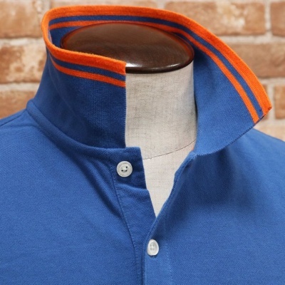 Polo azul com gola levantada com riscas alaranjada e azul escuro e botões brancos.