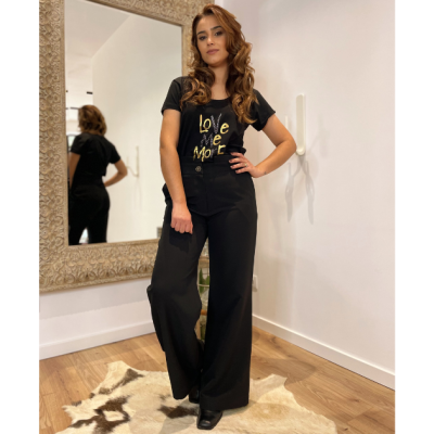 Mulher com calças pretas largas e t-shirt preta com texto amarelo