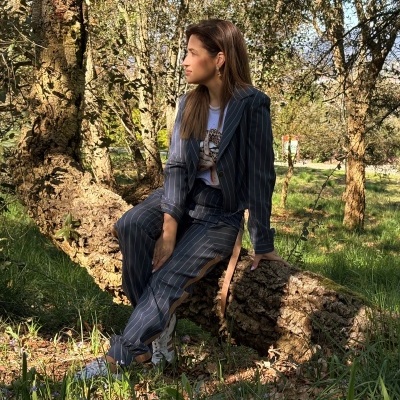 Mulher sentada num tronco em floresta com fato riscado azul e sapatilhas brancas