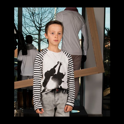 Camisola com estampa preta de silhuetas e mangas às riscas, num ambiente interior com manequins e espelho.