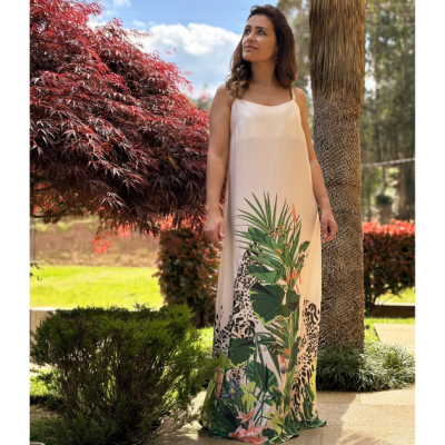 Vestido longo branco com estampa de folhas e flores na parte inferior, usado por mulher ao ar livre