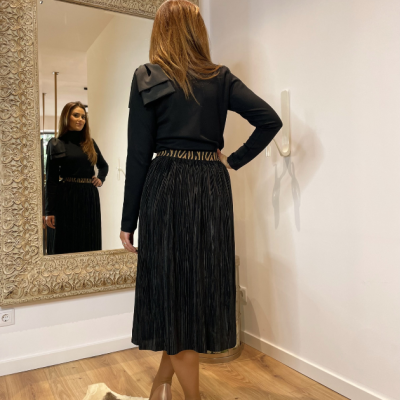 Mulher de costas com saia preta plissada e blusa preta, refletida em espelho decorativo