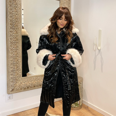 Mulher a usar casaco preto brilhante com pêlo branco nas golas e punhos, em interior moderno com espelho grande