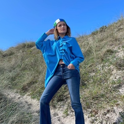 Mulher vestindo camisa azul com folhos e calças de ganga flange em dunas sob céu azul.