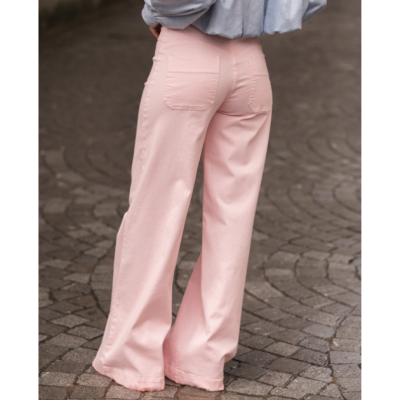 Calças de ganga rosa claras de corte largo vistas de trás em pavimento de calçada.