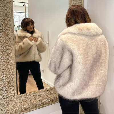 Mulher com casaco de pele sintética cremoso diante de espelho com moldura decorada