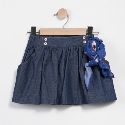 Saia azul escura com laço colorido pendurada em cabide de madeira.