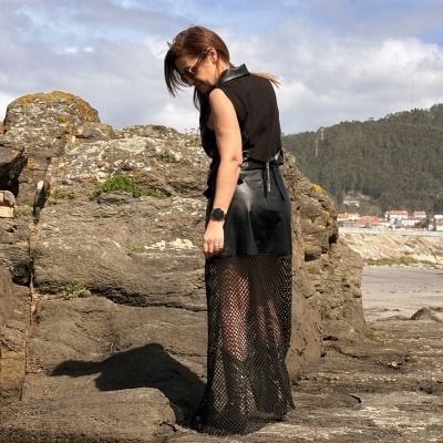 Mulher vestindo vestido preto transparente em rede junto a rochas na praia