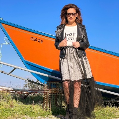 Mulher com casaco preto motard e saia com tule em frente a barco laranja