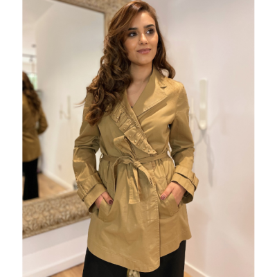 Casaco bege com cinto e detalhes franzidos usado por mulher em ambiente interior